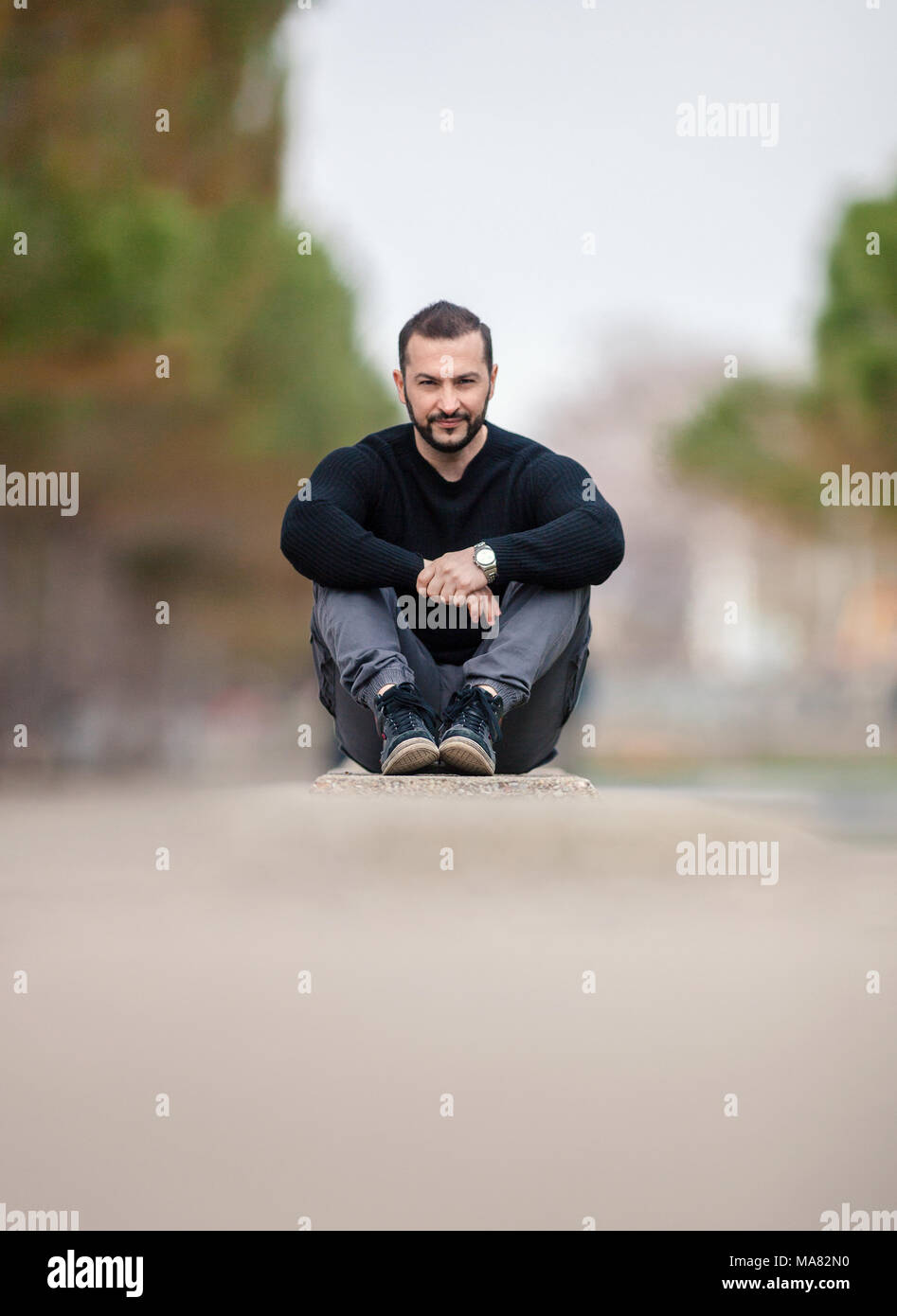 Successful Self Confident Man wearing casual clothes sitting on the ground at a park outdoors. Shot with extreme shallow depth of field using rare len Stock Photo
