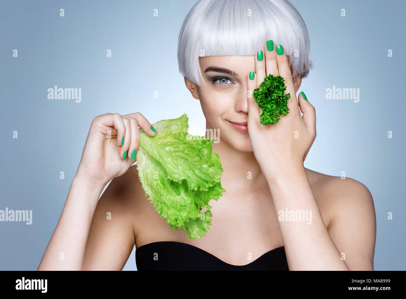 Beautiful blonde girl with parsley and lettuce leaves in her hand. Photo of fashion blonde girl on blue background. Healthy lifestyle concept Stock Photo