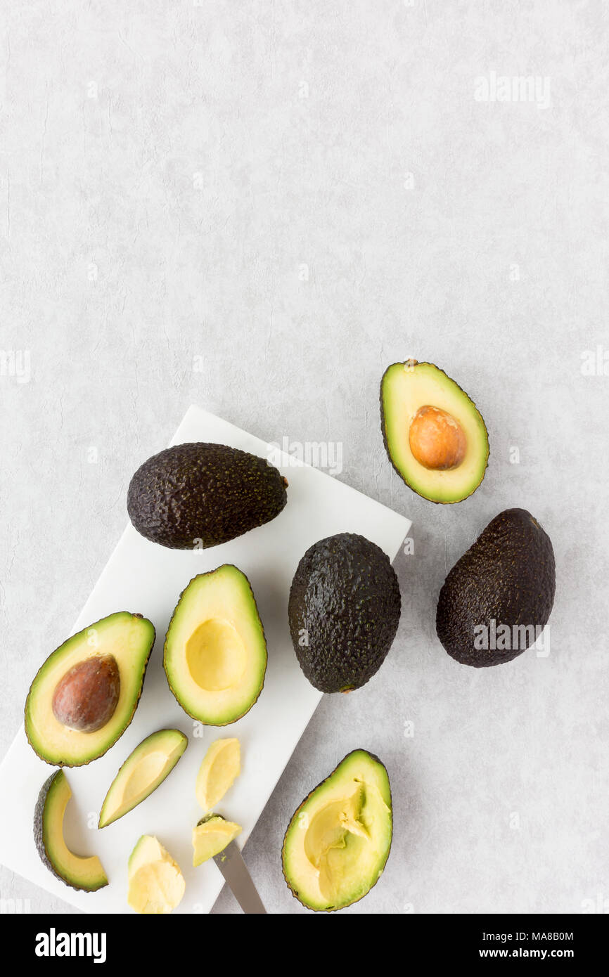Whole, halved and cut avocados scooped out with avocado scoop tool on marble chopping board. Top view. Stock Photo