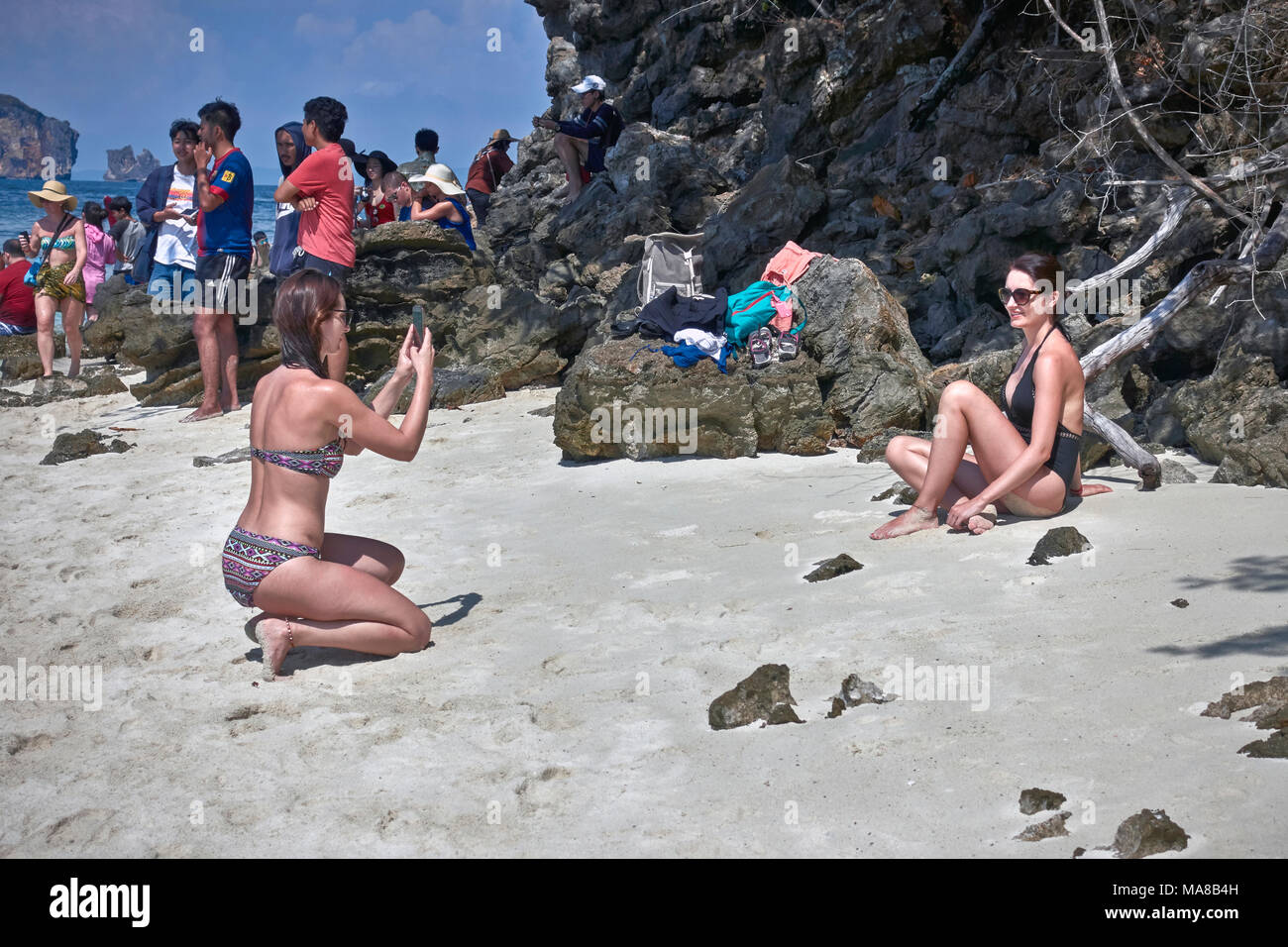 Woman taking a photograph of her female friend using a smartphone. Woman bikini beach. Stock Photo