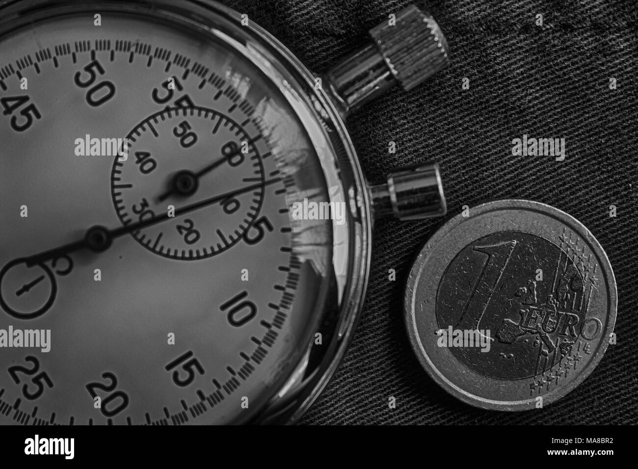 Euro coin with a denomination of one euro and stopwatch on old jeans backdrop - business background. Stock Photo