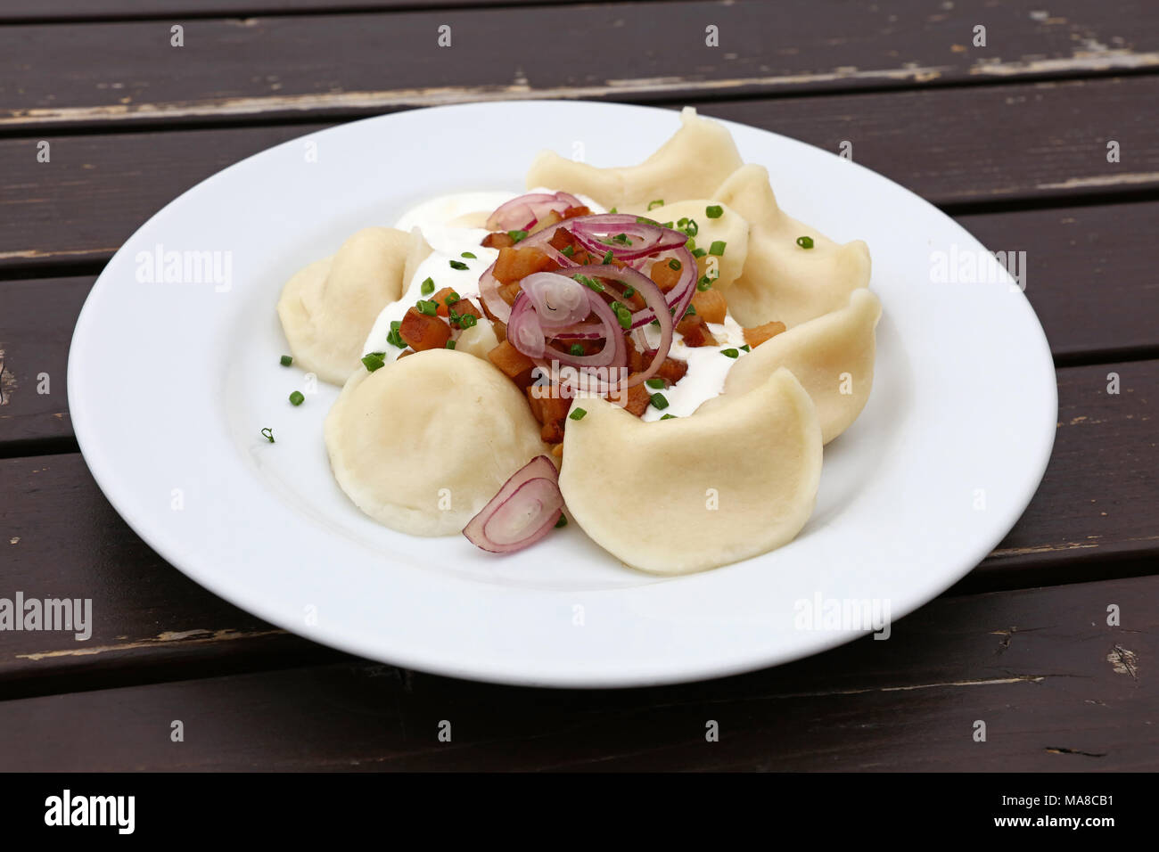 Plate of pierogi or varenyky stuffed filled dumplings with sour cream, bacon and onion, traditional East Europe cuisine meal popular in Poland, Ukrain Stock Photo