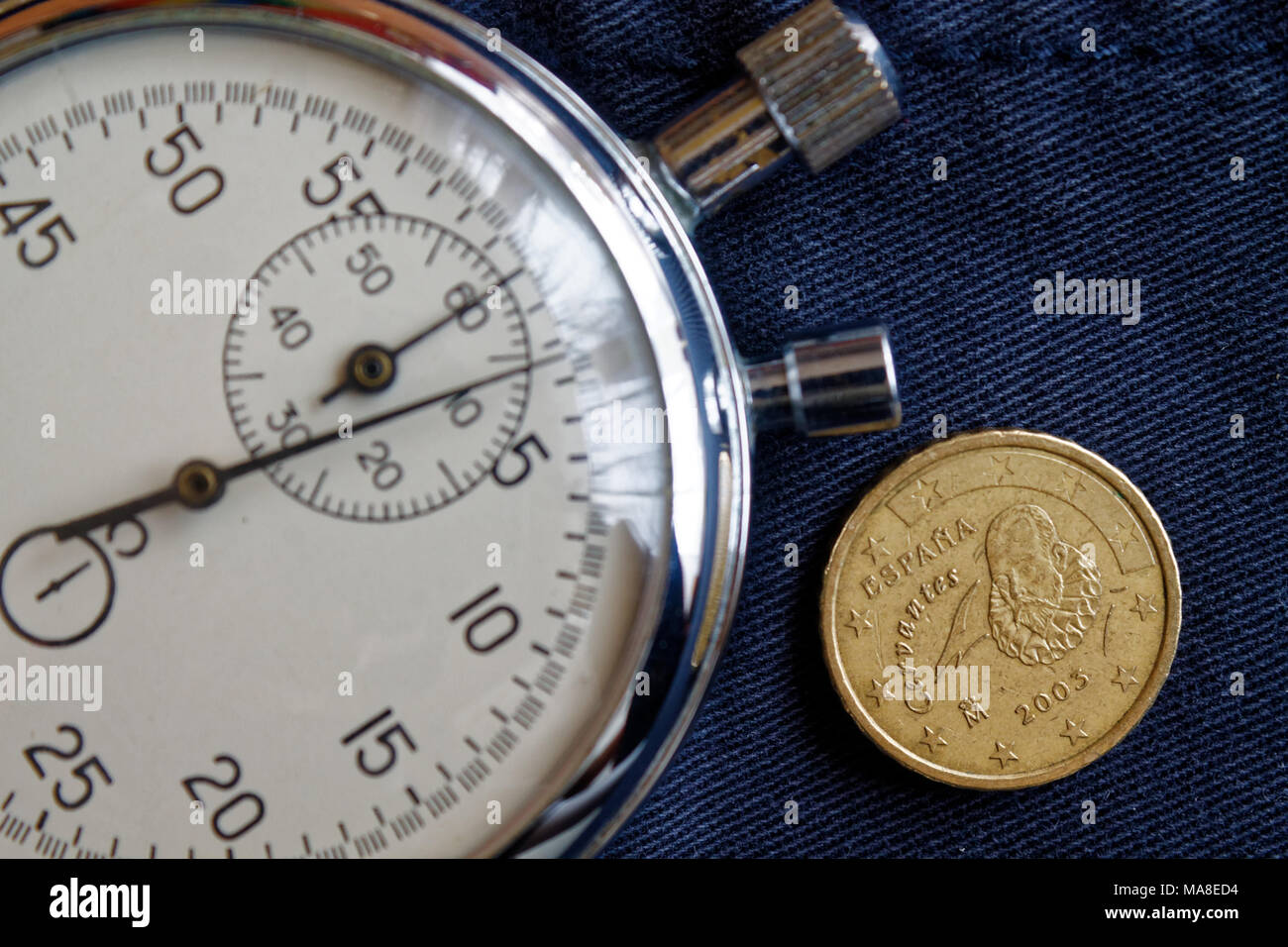 Euro coin with a denomination of 10 euro cents (back side) and stopwatch on old blue denim backdrop - business background Stock Photo