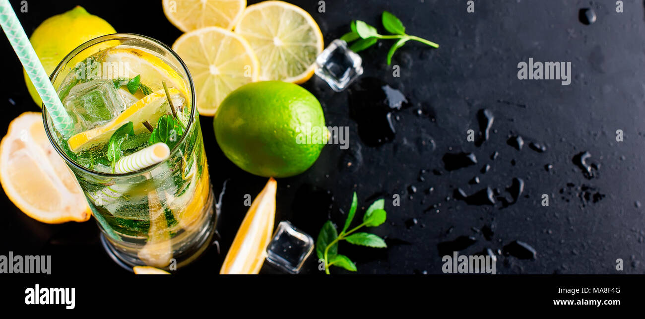 Top view of mojito cocktail, ice cubes and cocktail ingredients on black slate board, cocktail drinks concept. Banner. Stock Photo