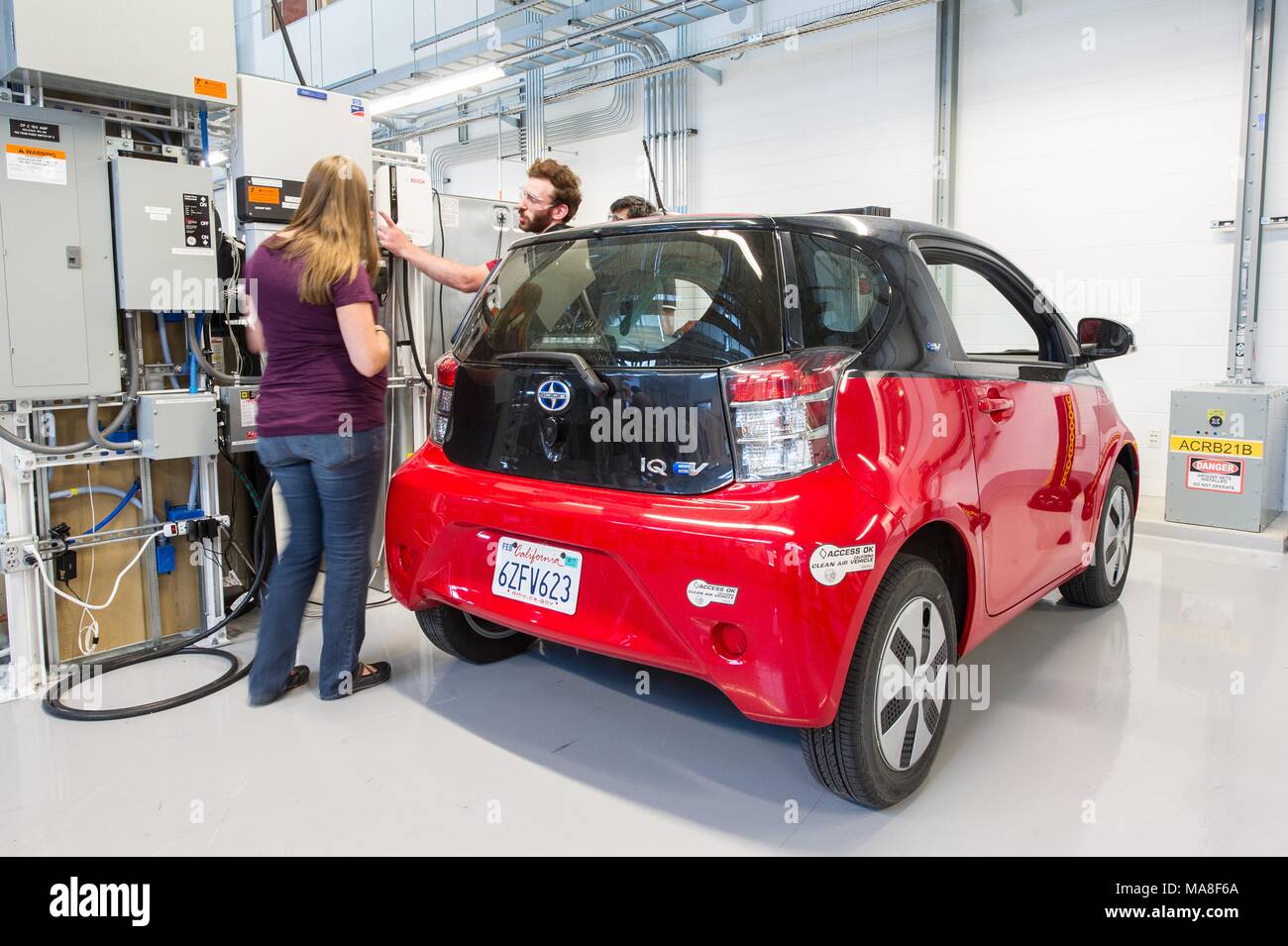 Three National Renewable Energy engineers work on the Electric Vehicle Supply Equipment (EVSE) and PV inverter as part of a 'smart-home-in-the-loop experiment, ' using a red, Toyota Scion, electric car, parked in a laboratory, at the Systems Performance Lab at the Energy Systems Integration Facility (ESIF), image courtesy of the US Department of Energy, July 11, 2016. () Stock Photo