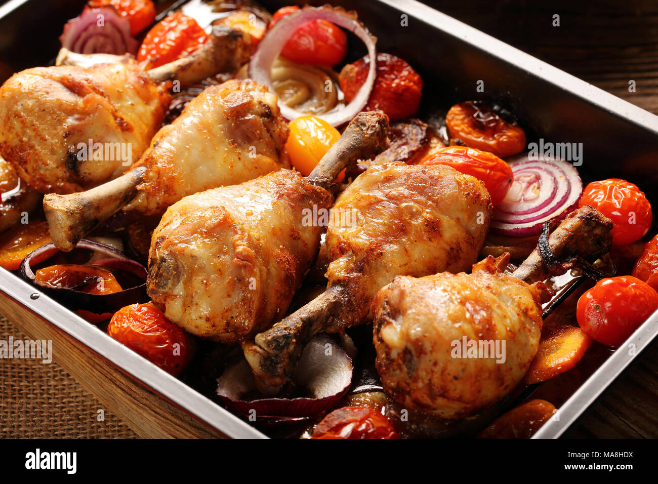 Roasted chicken legs with vegetables on wooden background Stock Photo