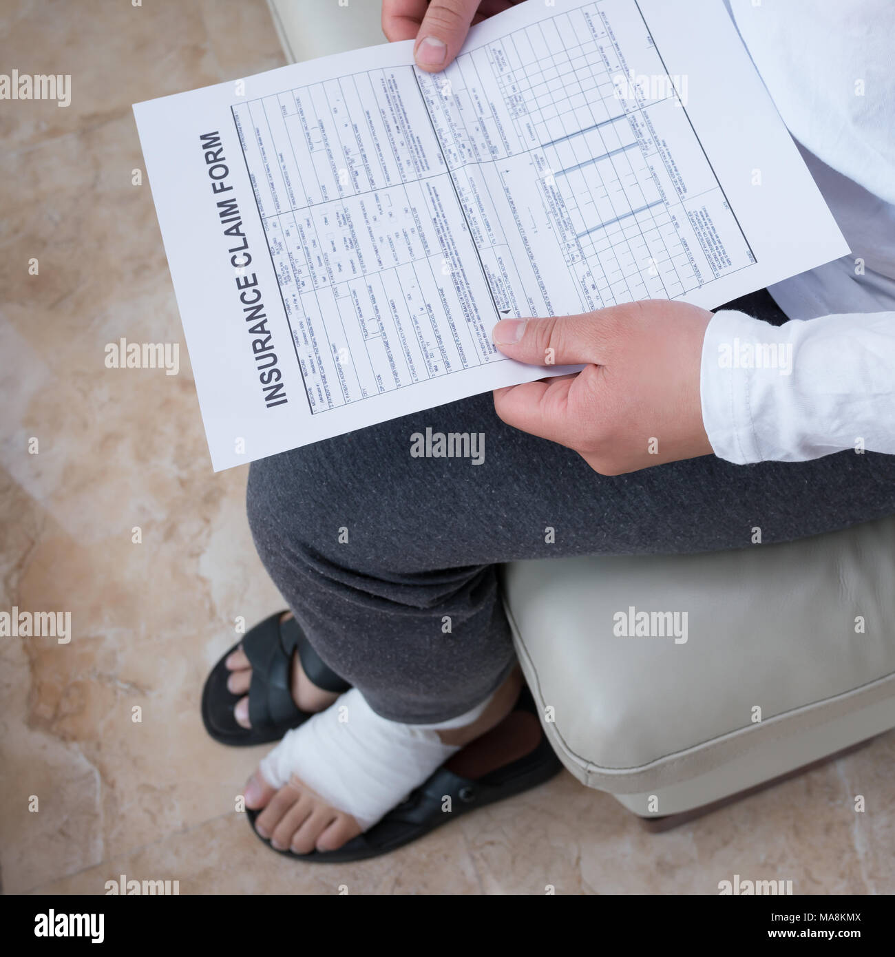 man with a wrapped foot sitting on sofa reading the work insurance claim form Stock Photo Alamy