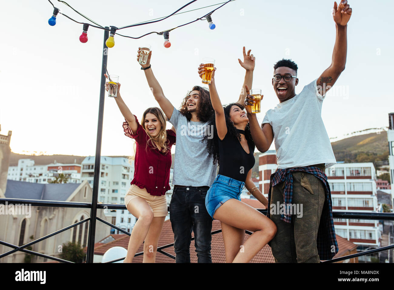 Friends enjoying and having fun at rooftop. Multiracial men and woman having party on rooftop in evening. Stock Photo