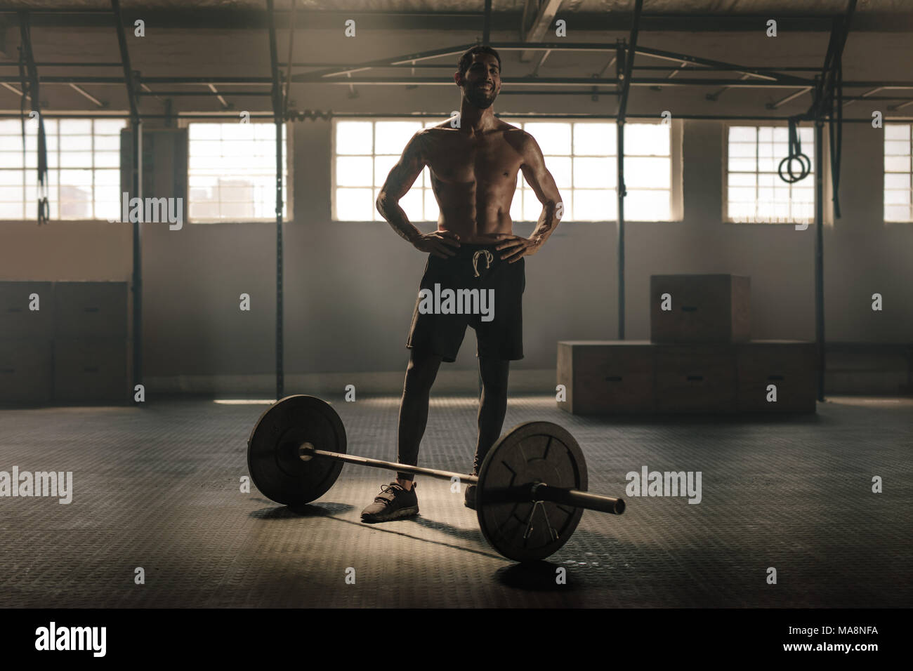 Muscular man standing with barbell on floor after workout in gym. Male