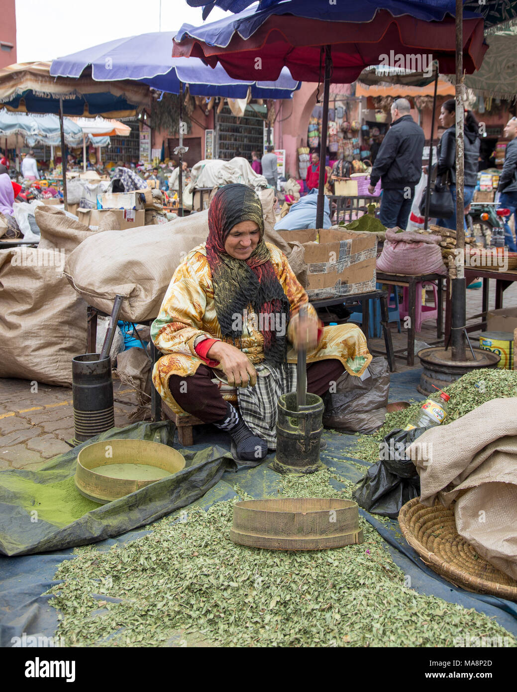 A woman market trader crushes by stamping and then sieving dried henna leaves to make a powder of the Henna dye Stock Photo