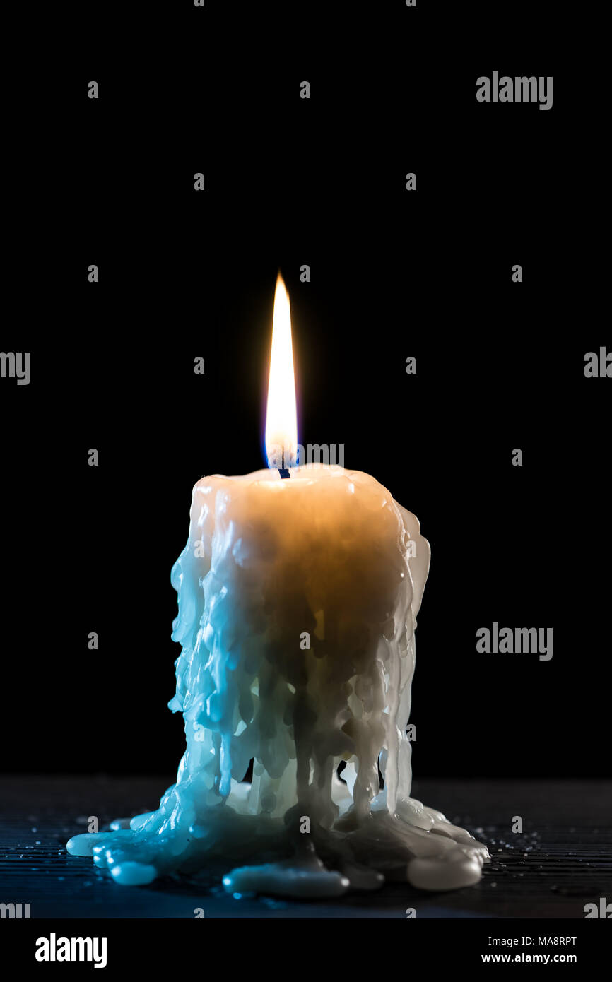 Single burning candle. Light of flame and flowing candle wax, dark