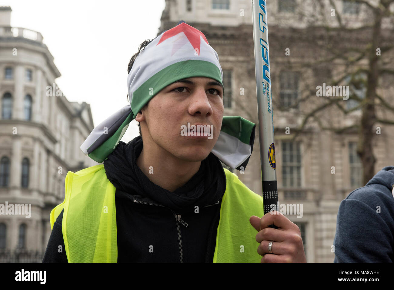 A young Syrian man, wearing Syrian flag over the head, is protesting against the Assad regime outside the Downing Street in London, UK. Stock Photo