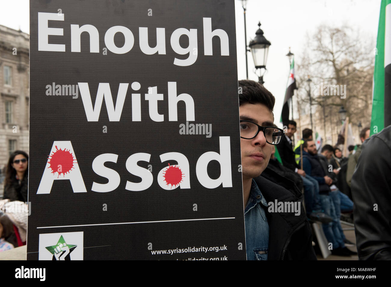 A young Syrian protester is holding a placard reading: 'Enough With Assad' outside the Downing Street in London, UK. Stock Photo