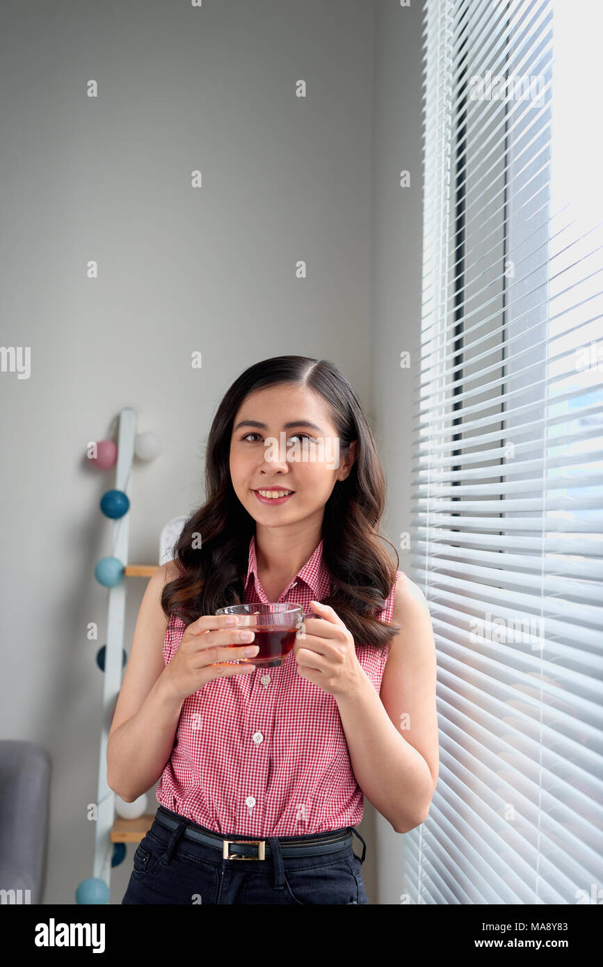 Young woman taking a tea break standing by the office window Stock