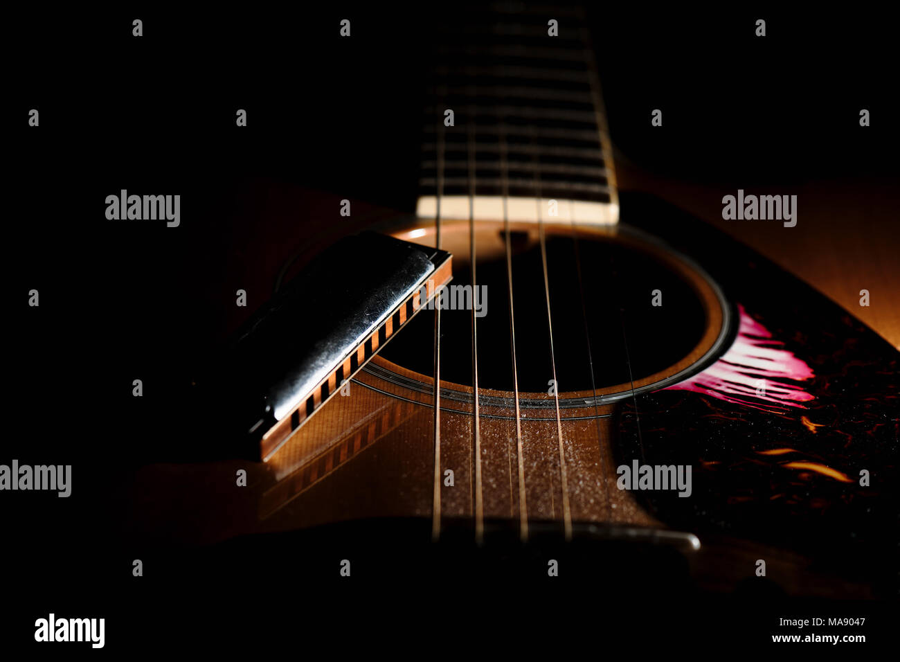 Detail of a blues harmonica near the sound hole of an acoustic guitar. Stock Photo