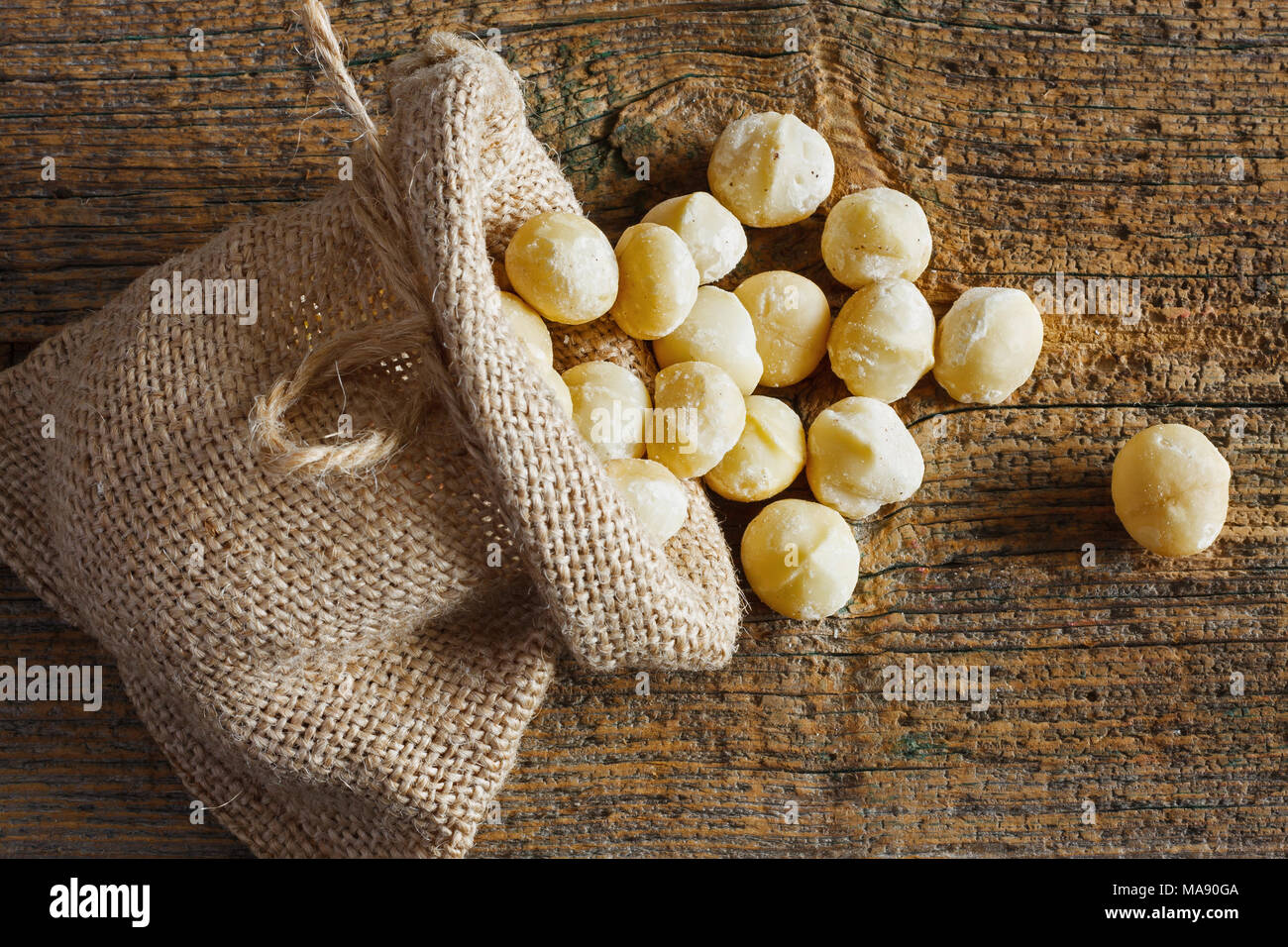 Macadamia nuts in small sack on wooden background Stock Photo