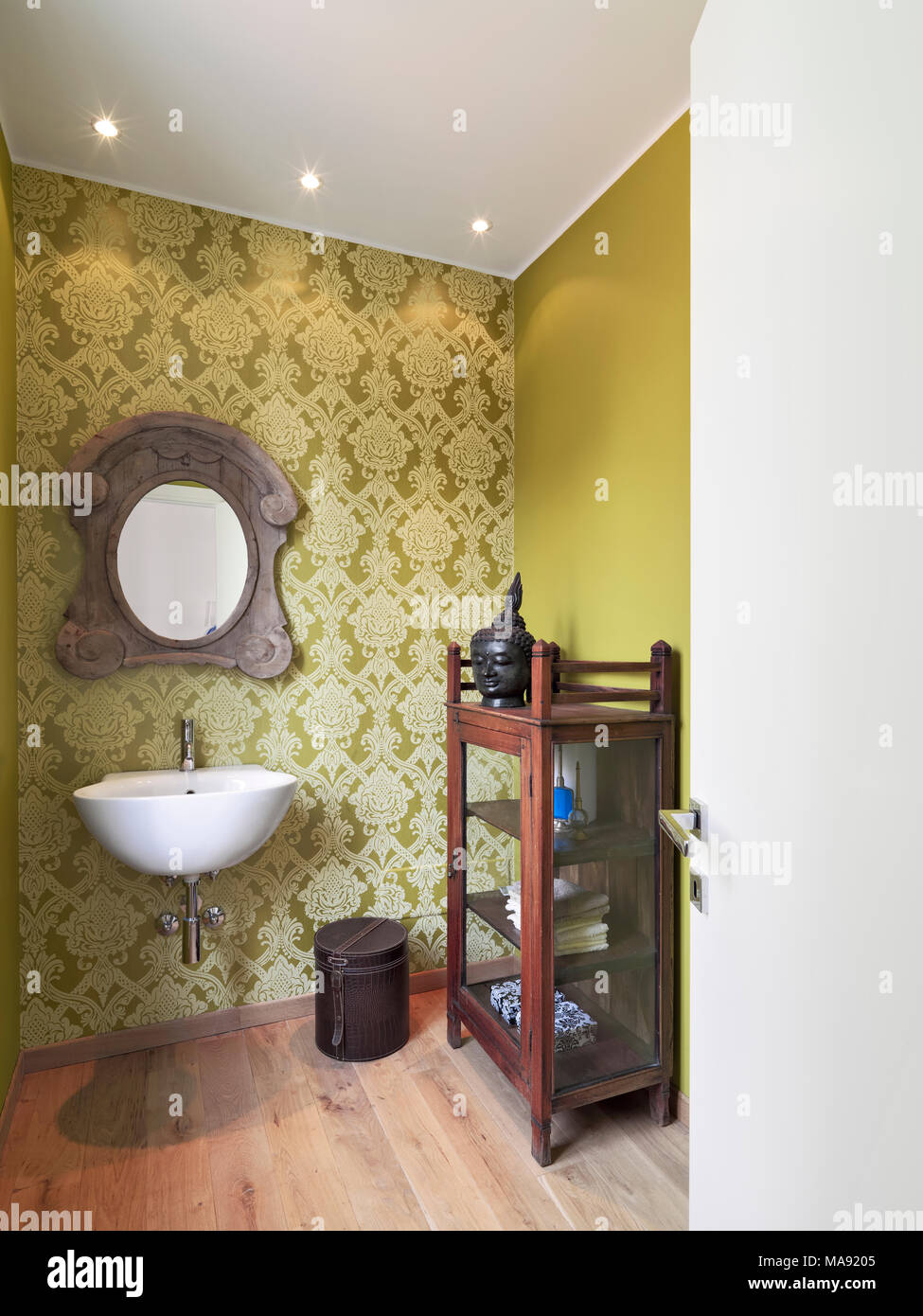 interiors shots of a bathroom with the wall-mounted washbasin the wallpaper and the green wall the floor is made of wood Stock Photo
