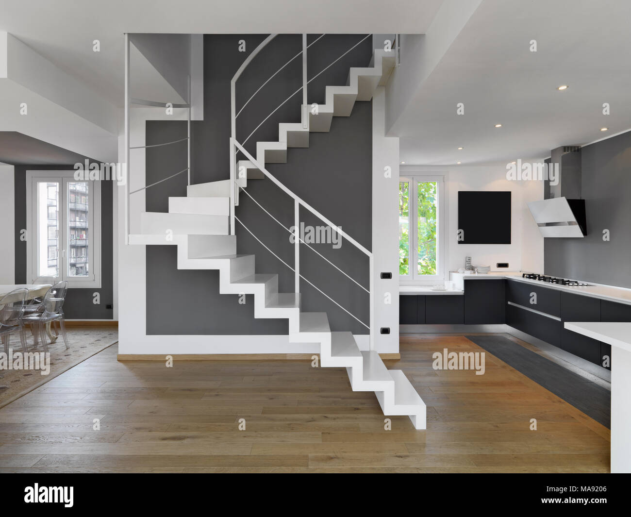interior shots of a modern apartment overlooking on the kitchen and the dining room in foreground the staircase wjose floor is made of wood Stock Photo