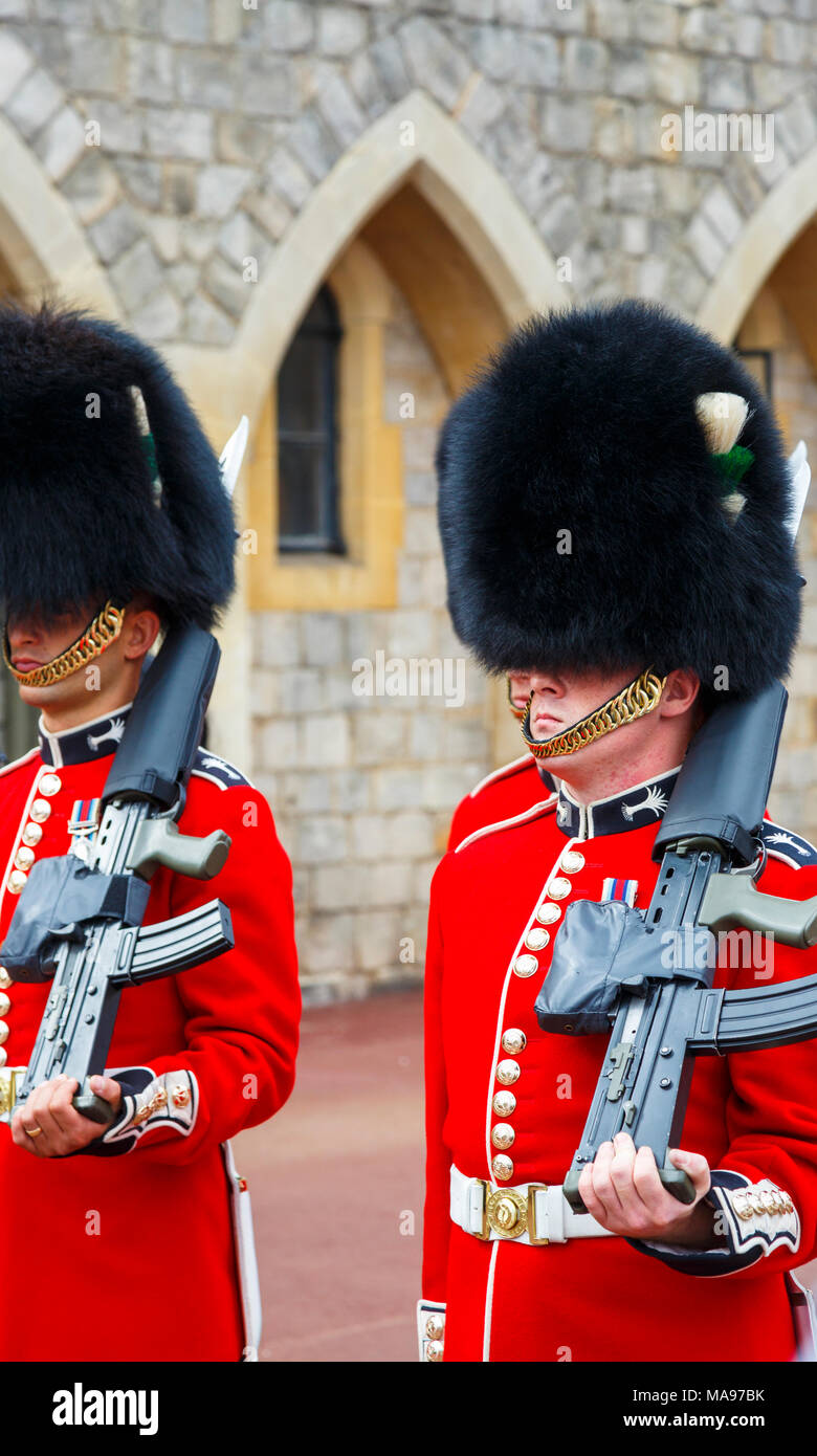 Soldiers in Queen's Guard at Windsor Castle, England, with red uniform and traditional black bearskin cap or busby marching with shouldered arms Stock Photo