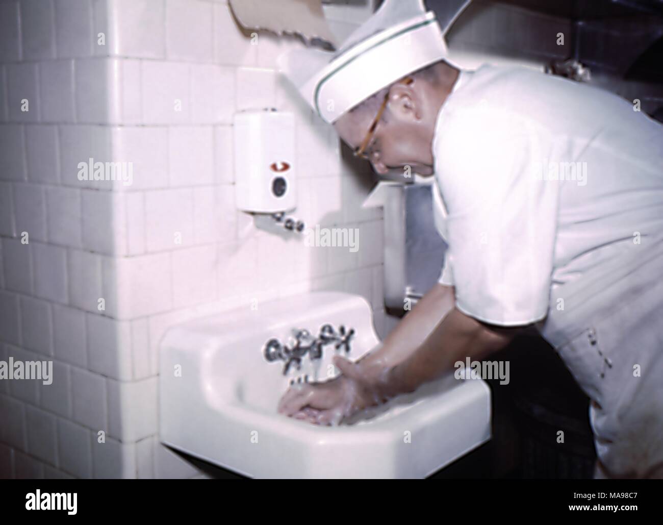 Photograph of a chef in uniform, washing his hands prior to preparing food at a migrant labor work camp, 1975. Image courtesy CDC. () Stock Photo