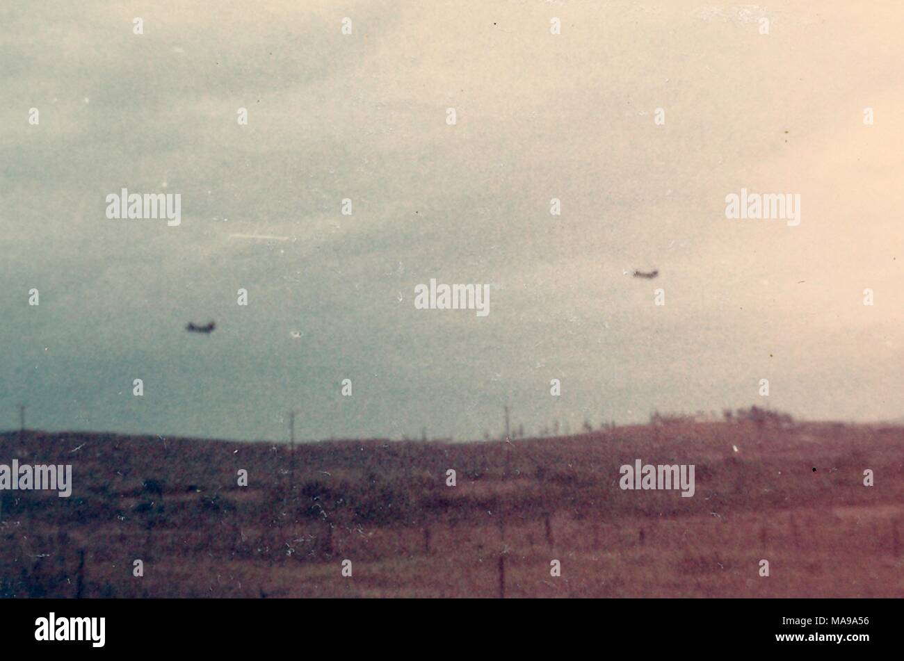 Color photograph, showing a pair of tandem rotor helicopters flying low