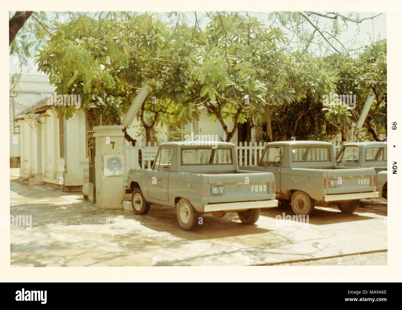 Color photograph, showing three Ford pickup trucks parked in front of a picket fence, with trees and a white house in the background, photographed in Vietnam during the Vietnam War (1955-1975), 1968. () Stock Photo