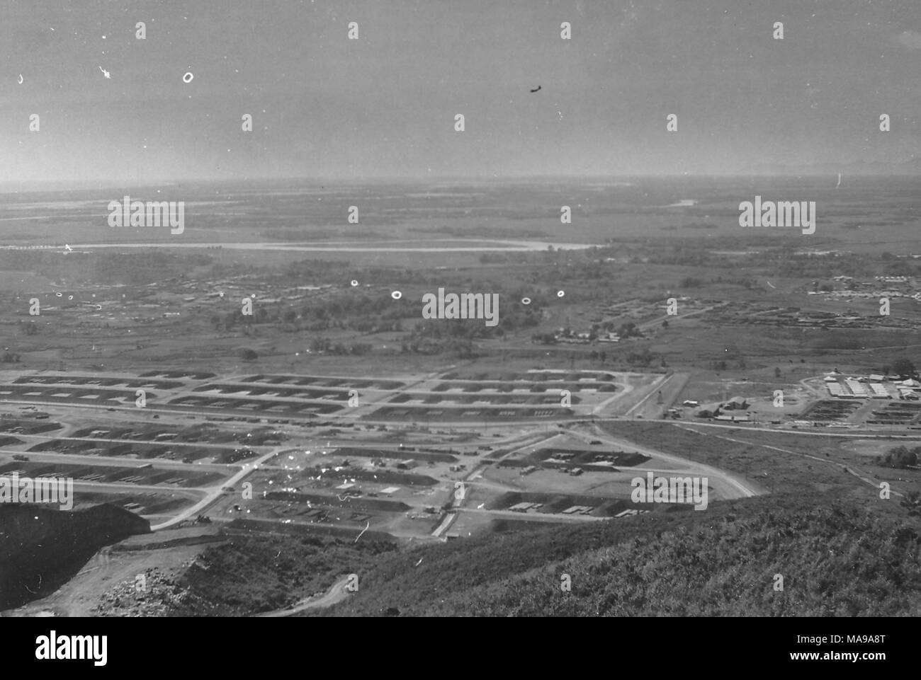 Black and white photograph showing an aerial view, or a view shot from a hill, over a flat landscape, with roads or landing strips, and several buildings, likely the barracks of the US Marine Corps camp, located at midground, photographed in Vietnam during the Vietnam War (1955-1975), 1968. () Stock Photo