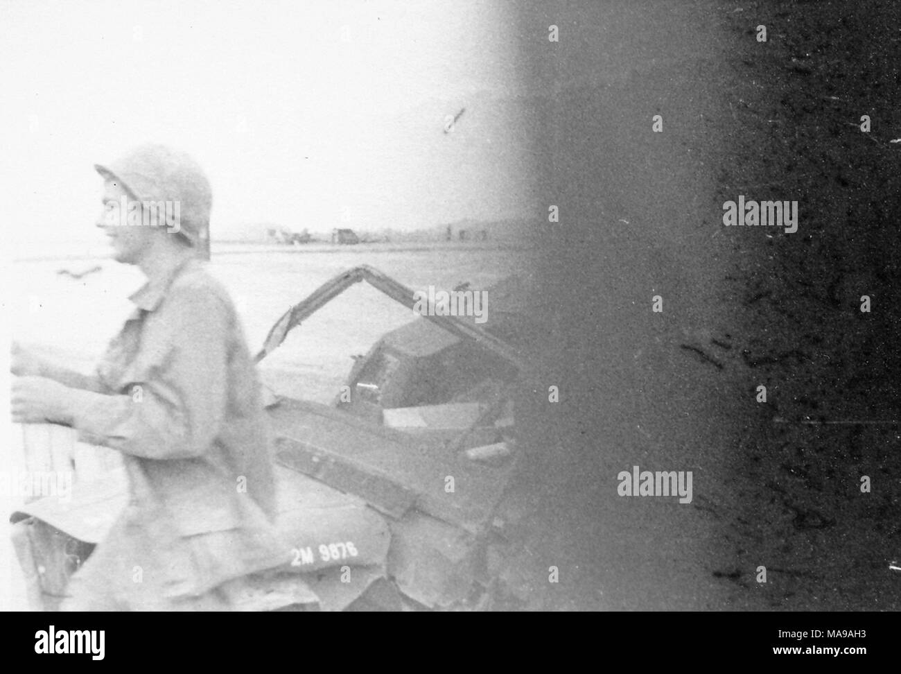 Black and white photograph, partially obscured, showing a soldier, in three-quarter profile, wearing a helmet and fatigues, walking past the hood of a military vehicle, photographed in Vietnam during the Vietnam War (1955-1975), 1971. () Stock Photo