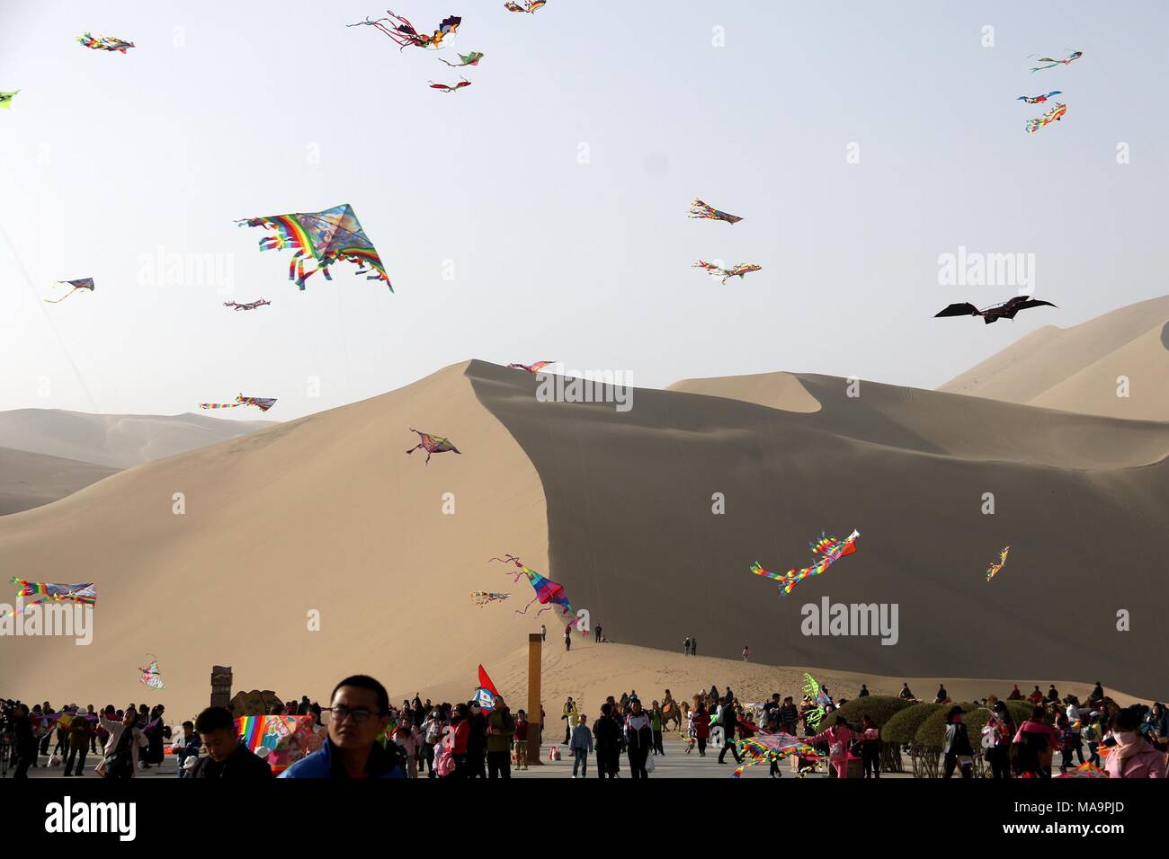 Dunhuang, China's Gansu province. 31st Mar, 2018. People fly kites at the scenic spot of the Crescent Spring, a crescent-shaped lake surrounded by deserts at the foot of the Mingsha Hill, in Dunhuang, northwest China's Gansu province, March 31, 2018. Credit: Zhang Xiaoliang/Xinhua/Alamy Live News Stock Photo
