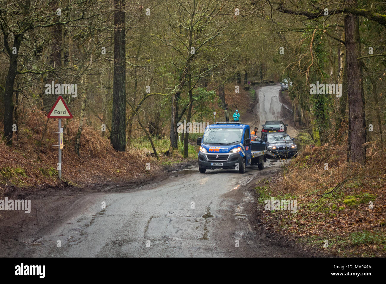 Frensham, Surrey, UK, Saturday 31st March 2018. After recent heavy rainfall a recovery truck attends to a BMW that has broken down after driving through the Ford at Grange Road, Frensham, Surrey, England. Stock Photo