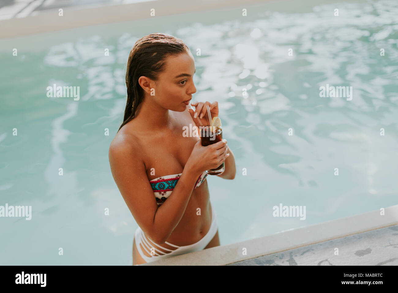 Young woman drinking coctail by swimming pool at hot summer day Stock Photo