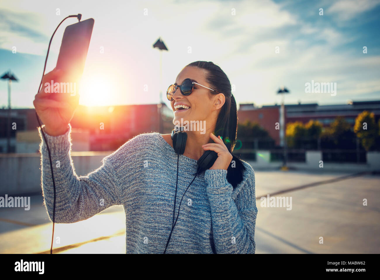 Young urban woman in casual wear selecting song on playlist in sunset, outdoors Stock Photo