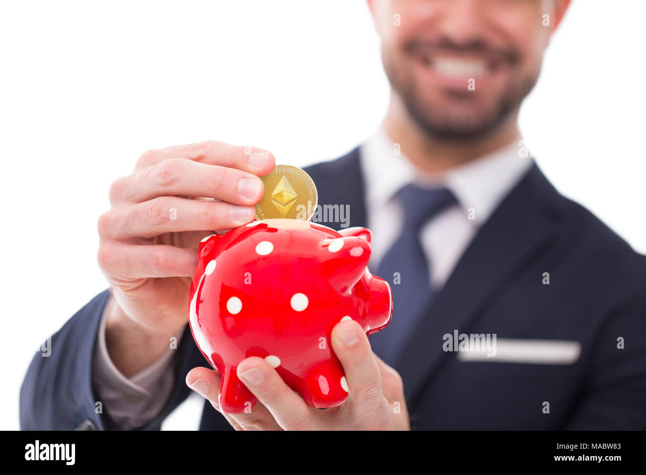 Young businessman drop ethereum into piggy bank, toothy smile, depth of field, isolated on white Stock Photo