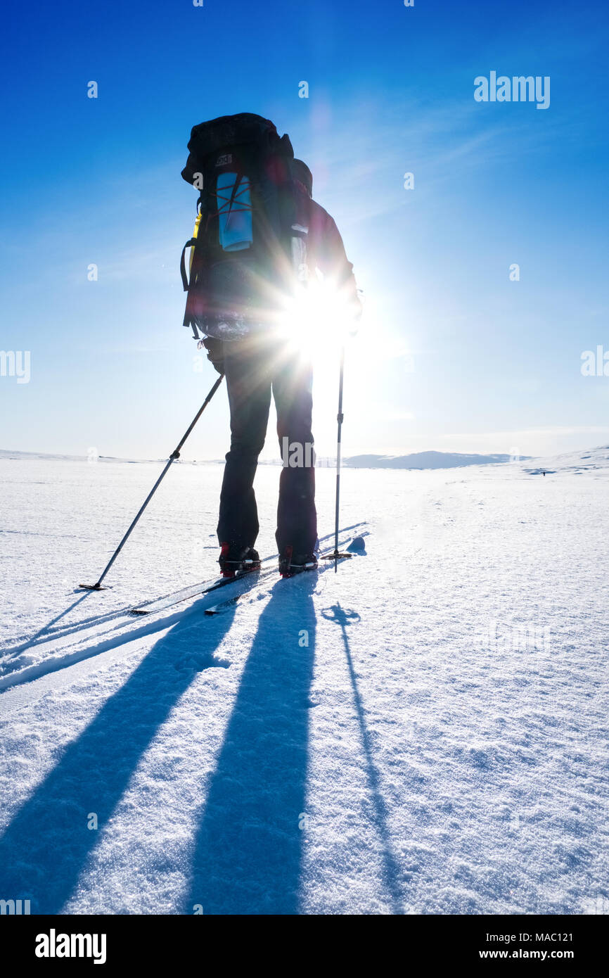 Single male photographed against bright winter sun whilst ski-touring in Northern Norway Stock Photo