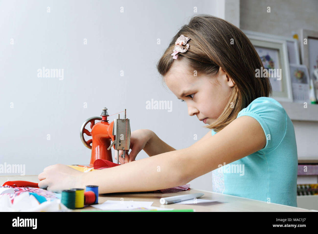 The girl is sitting at the table and sewing on a sewing machine. Stock Photo