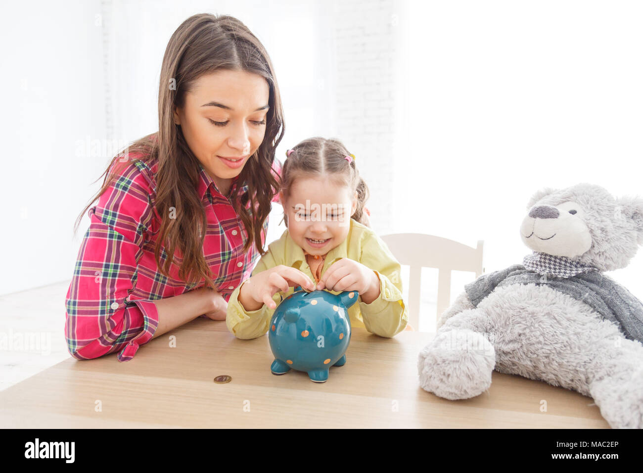 Mother and daughter putting coins into piggy bank Stock Photo - Alamy