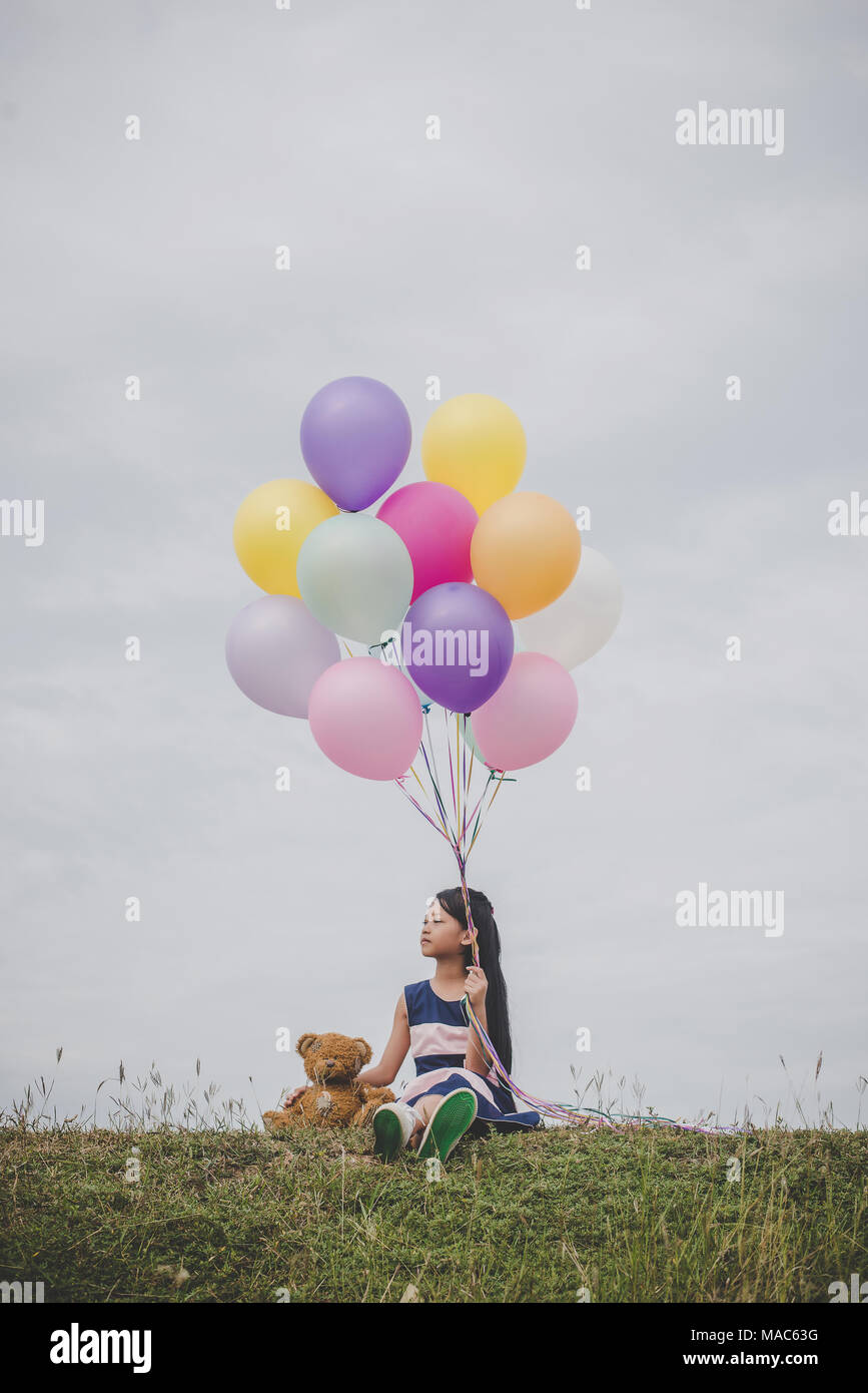 Little cute girl with teddy bear sitting on long green grass outside ...