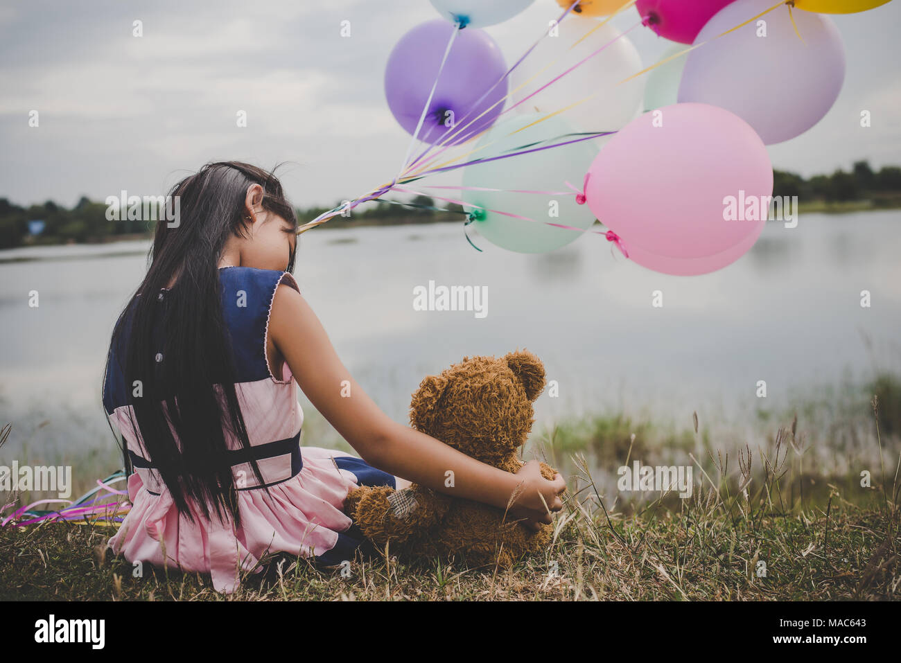 Little cute girl with teddy bear sitting on long green grass outside ...