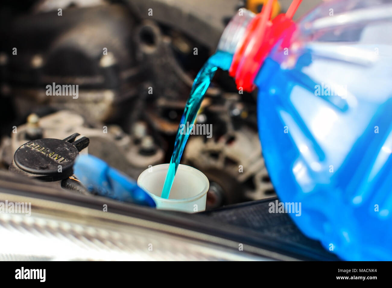Detail on antifreeze car screen wash liquid pouring into dirty car from blue and red anti freeze water container. Stock Photo