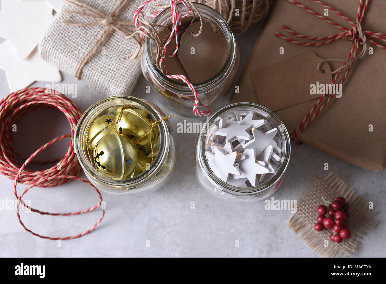 Christmas present wrapping supplies. High angle shot of three mason jars with gift tags, wood stars, and sleigh bells agains a rustic white wood wall. Stock Photo