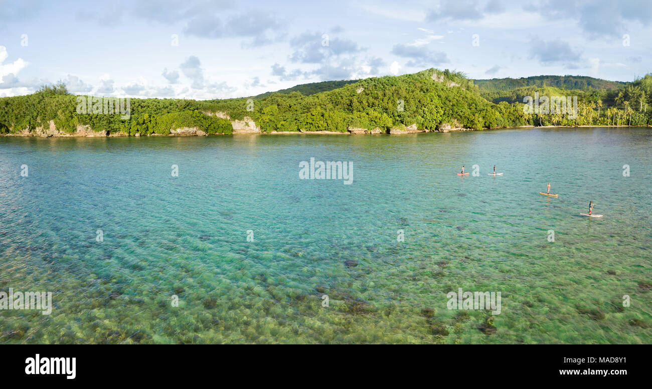An aerial panorama of four people on stand-up paddle boards on a calm day in Piti Bay, Guam, Micronesia, Mariana Islands, Pacific Ocean. Stock Photo