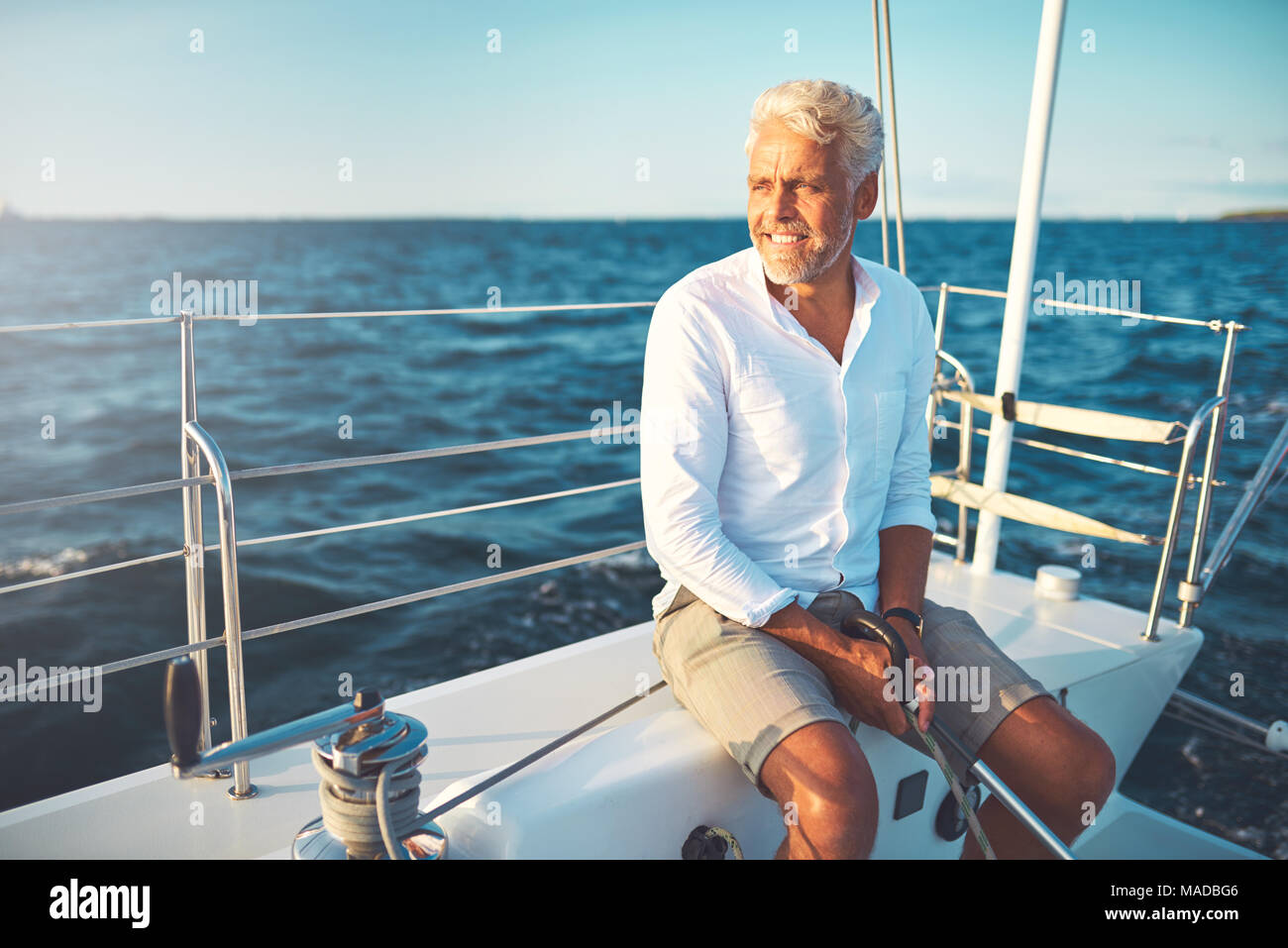 Mature man sitting on the deck of his boat enjoying a sunny day sailing ...