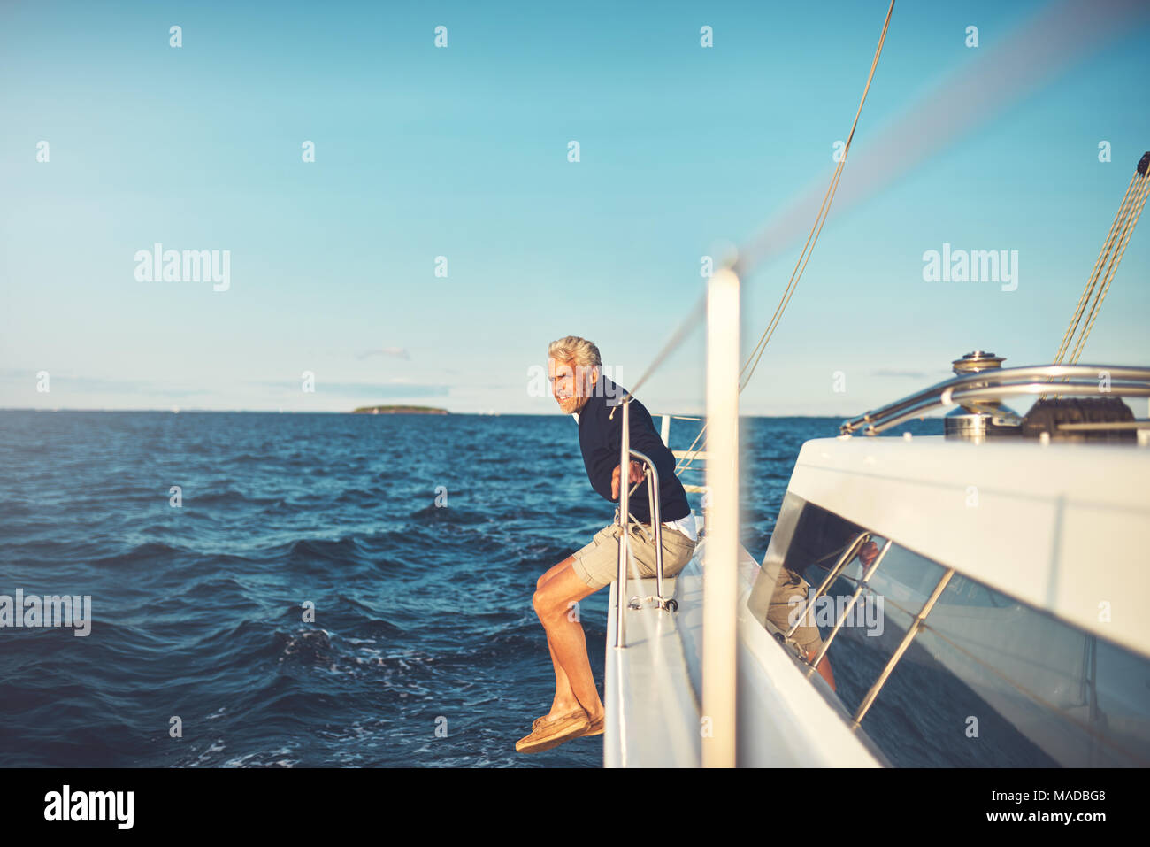Smiling mature man leaning on the railing of his boat while enjoying a ...