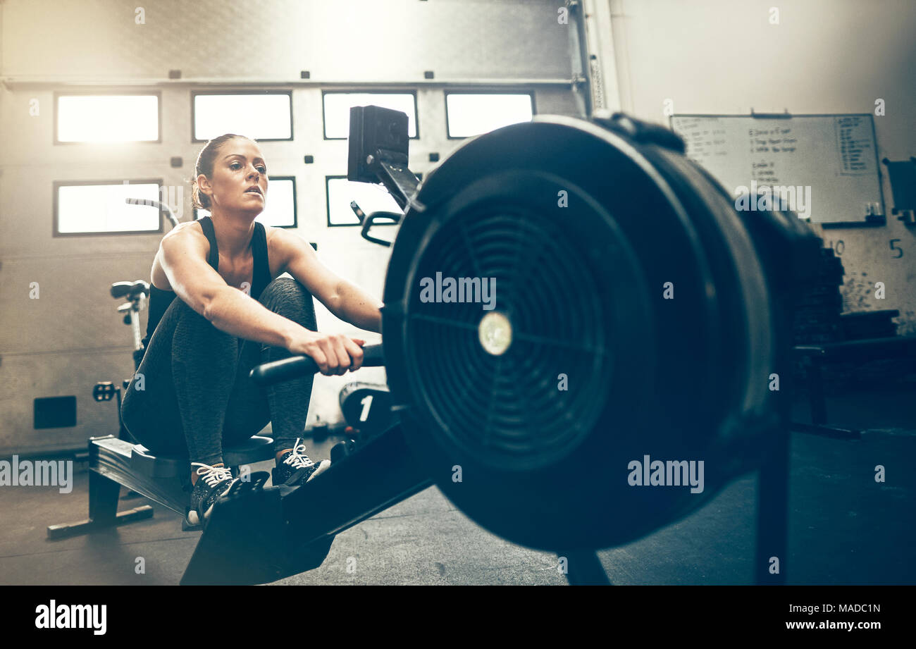 Fit young woman exercising on a rowing machine during a workout session ...