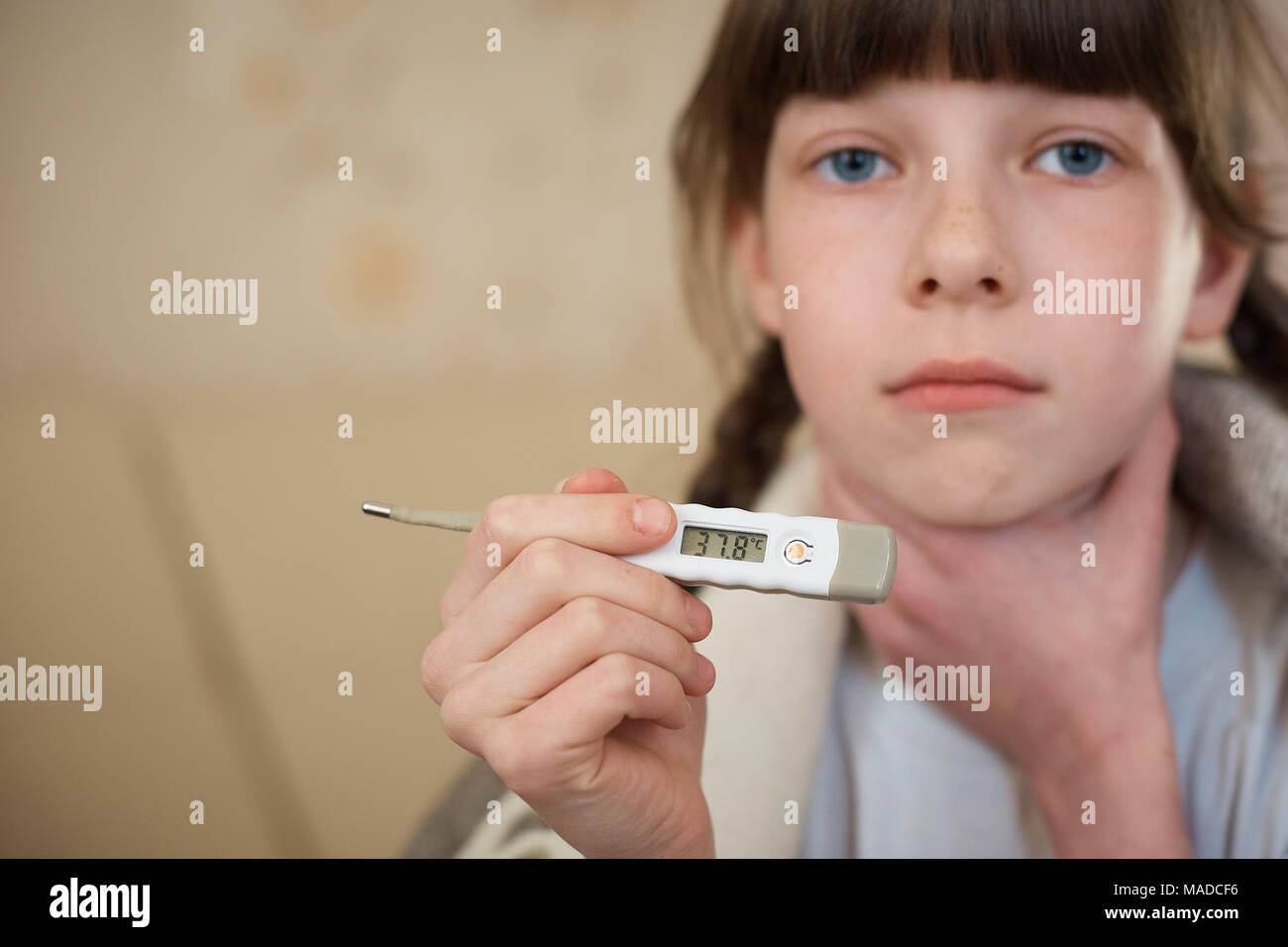 Little baby girl in pink bathrobe holding a digital thermometer with high temperature, close-up shot Stock Photo