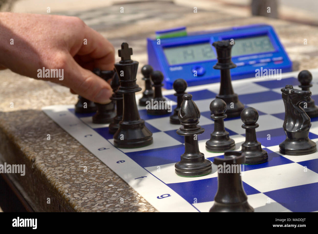 Close up of a white man's hand moving a black chess piece on a blue and