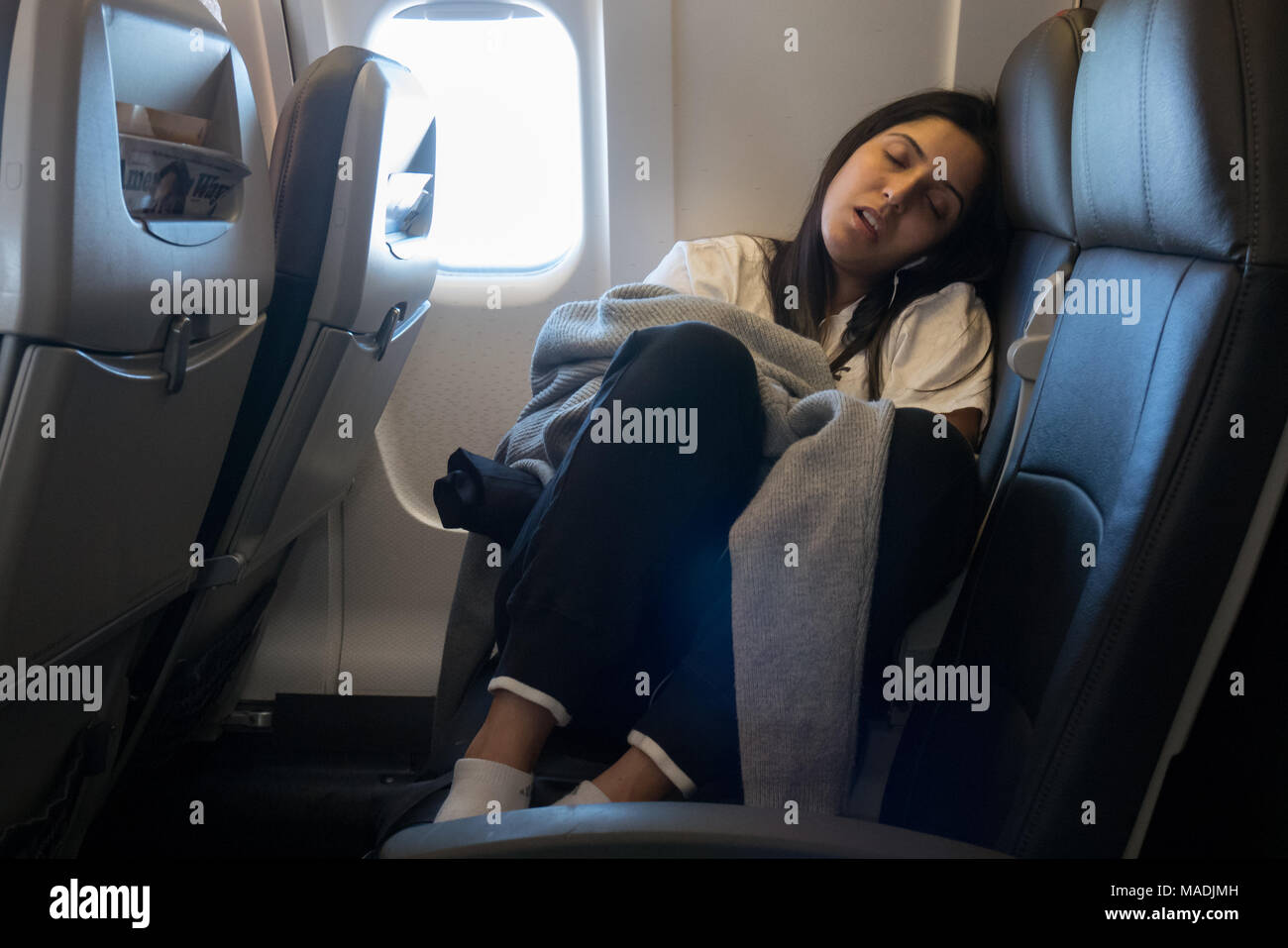 female passenger sleeping inside airplane taking up two seats Stock Photo