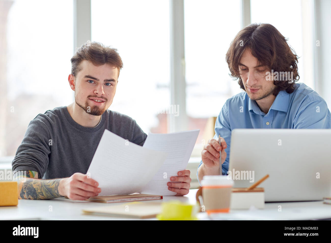 Portrait of two partners sitting with documents and using laptop Stock Photo