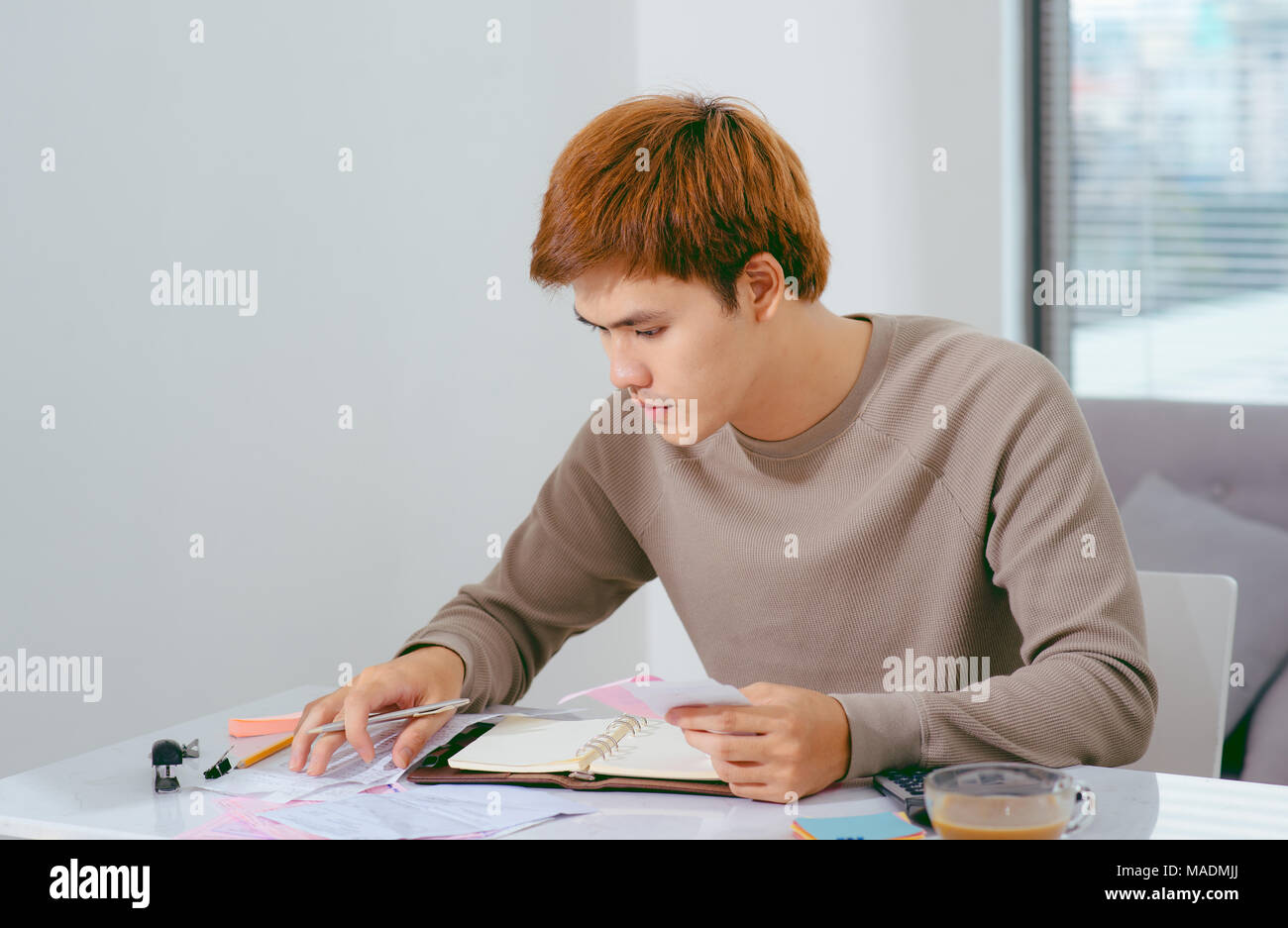 young attractive Young Asian man at home sitting on sofa with calculator accounting costs, charges, taxes and mortgage for paying bills looking worrie Stock Photo