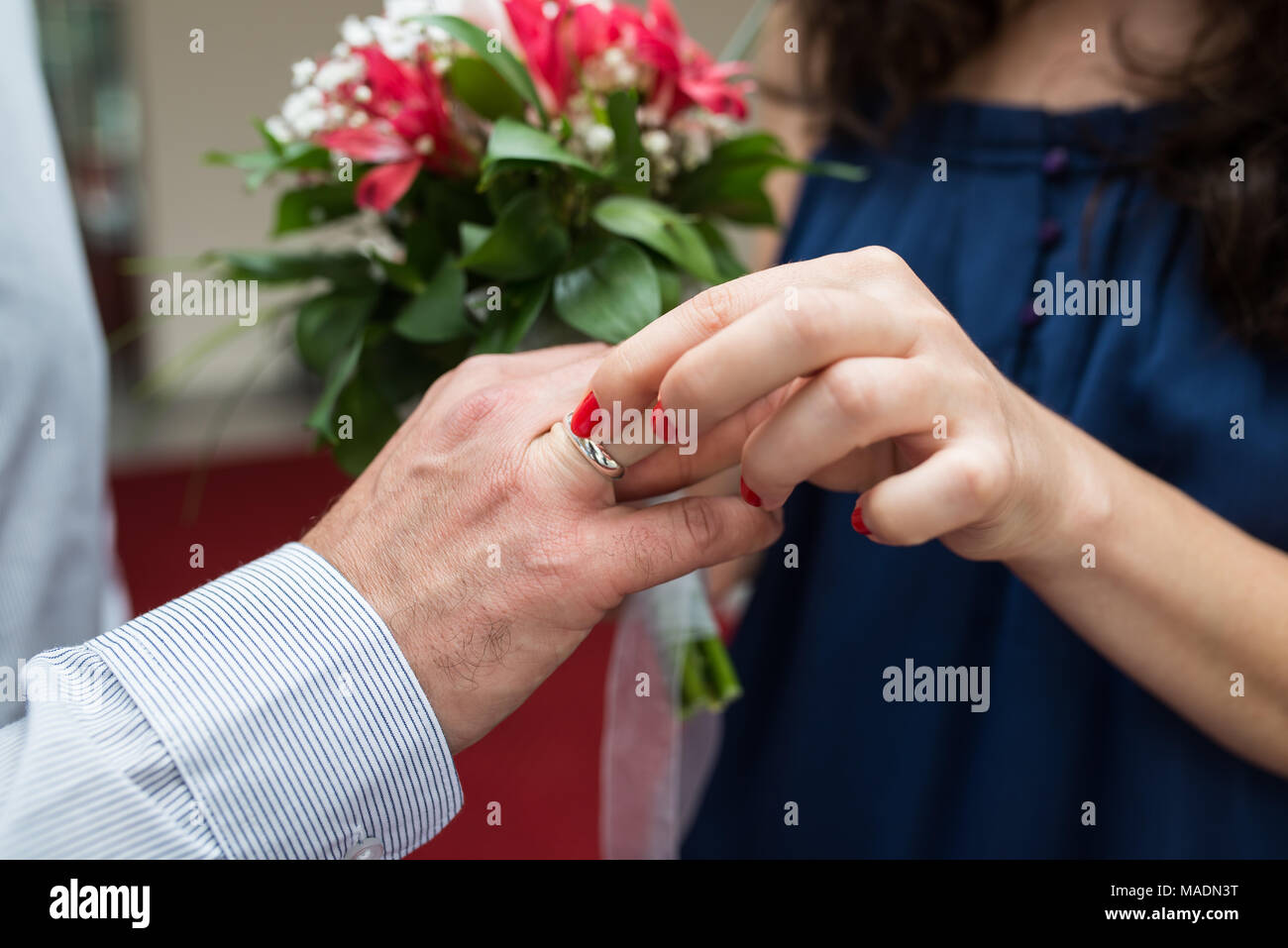 A closeup of a bride putting a wedding band on the groom’s finger Stock Photo